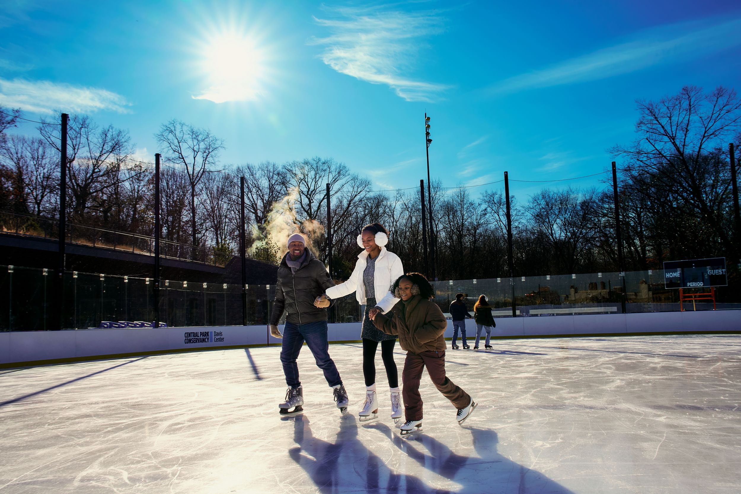 Family holds hands and skates on the ice rink at the Davis Center in Harlem, NYC
