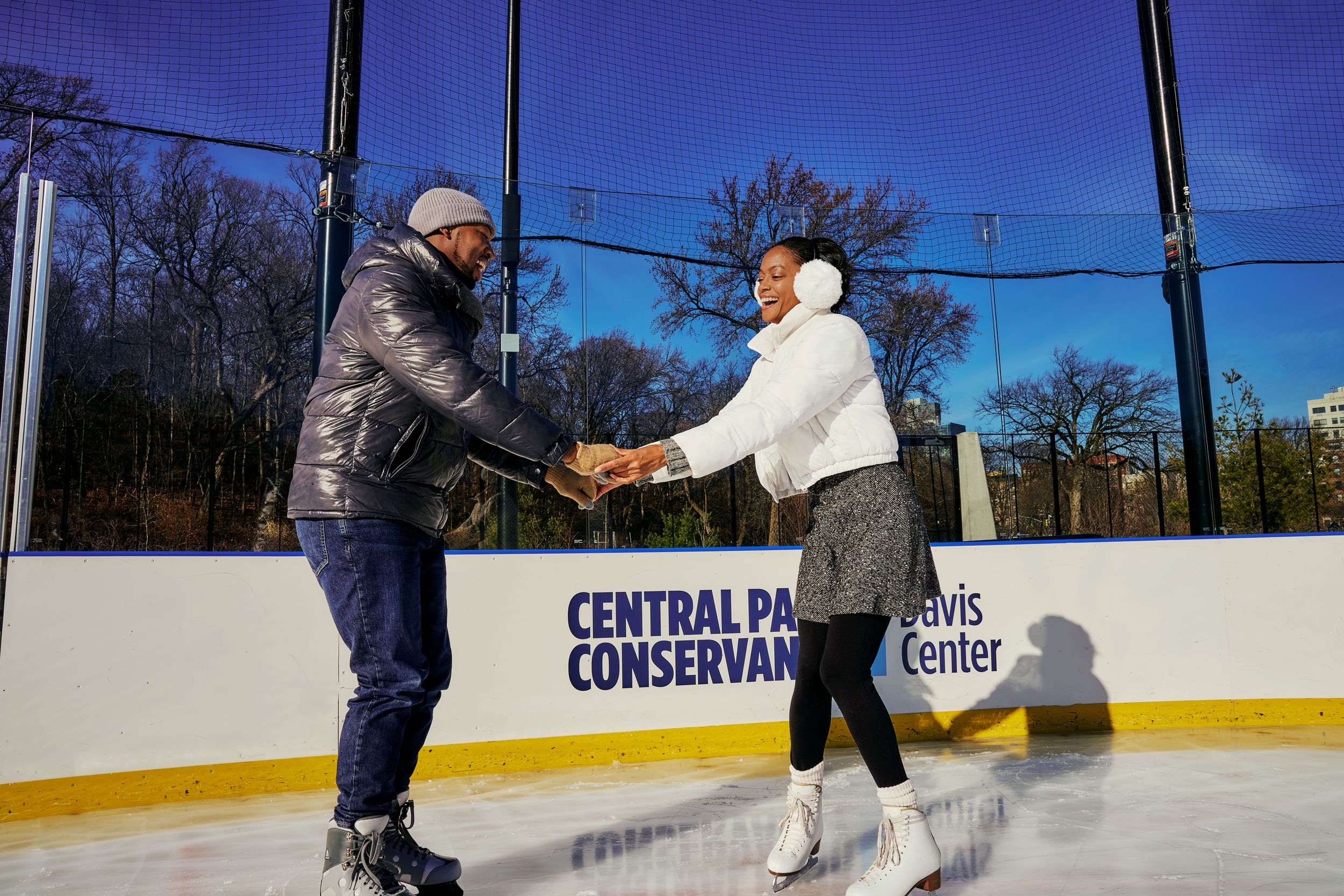 Smiling couple holding hands while skating on the ice rink