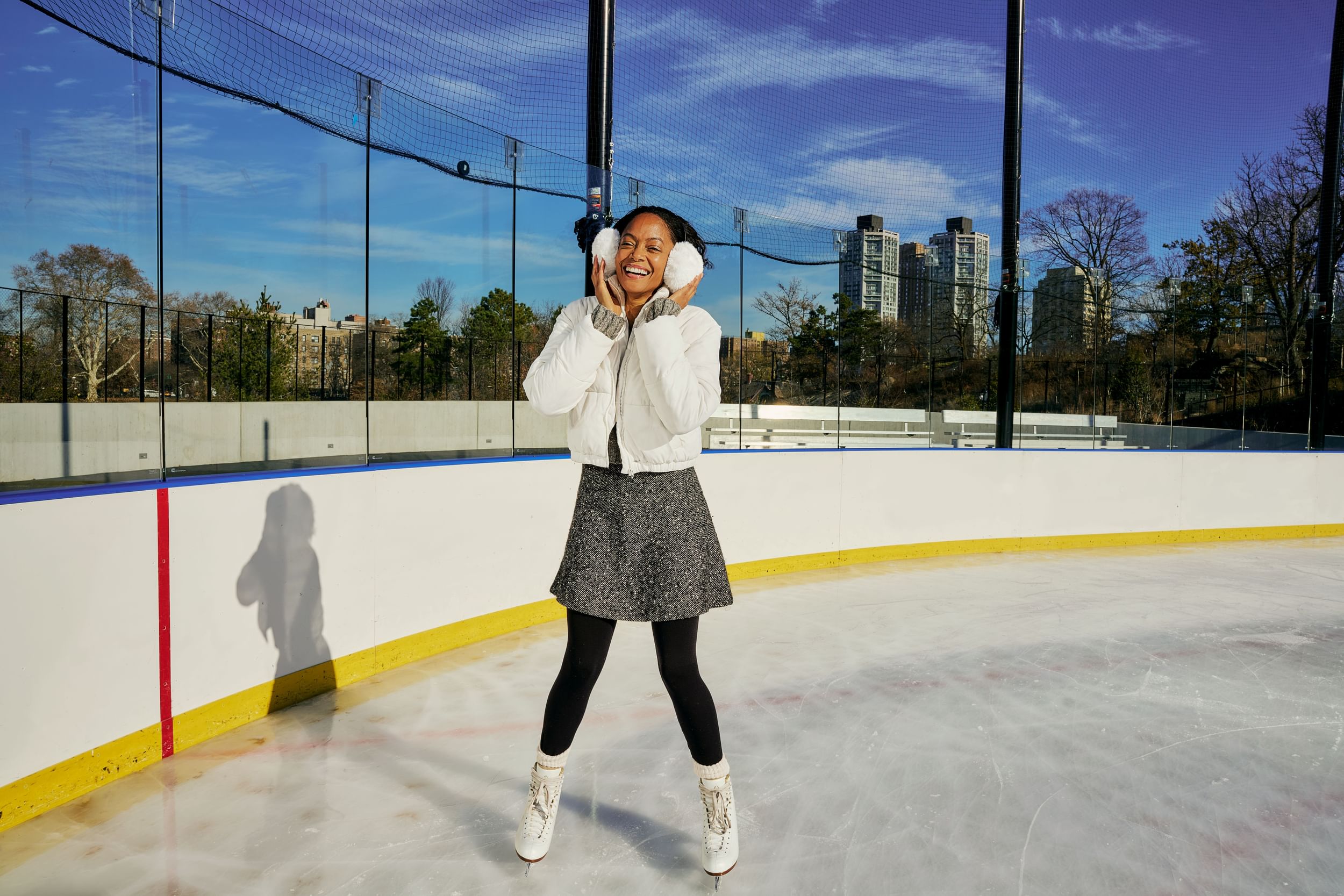 Woman on the ice rink smiling at camera and holding earmuffs