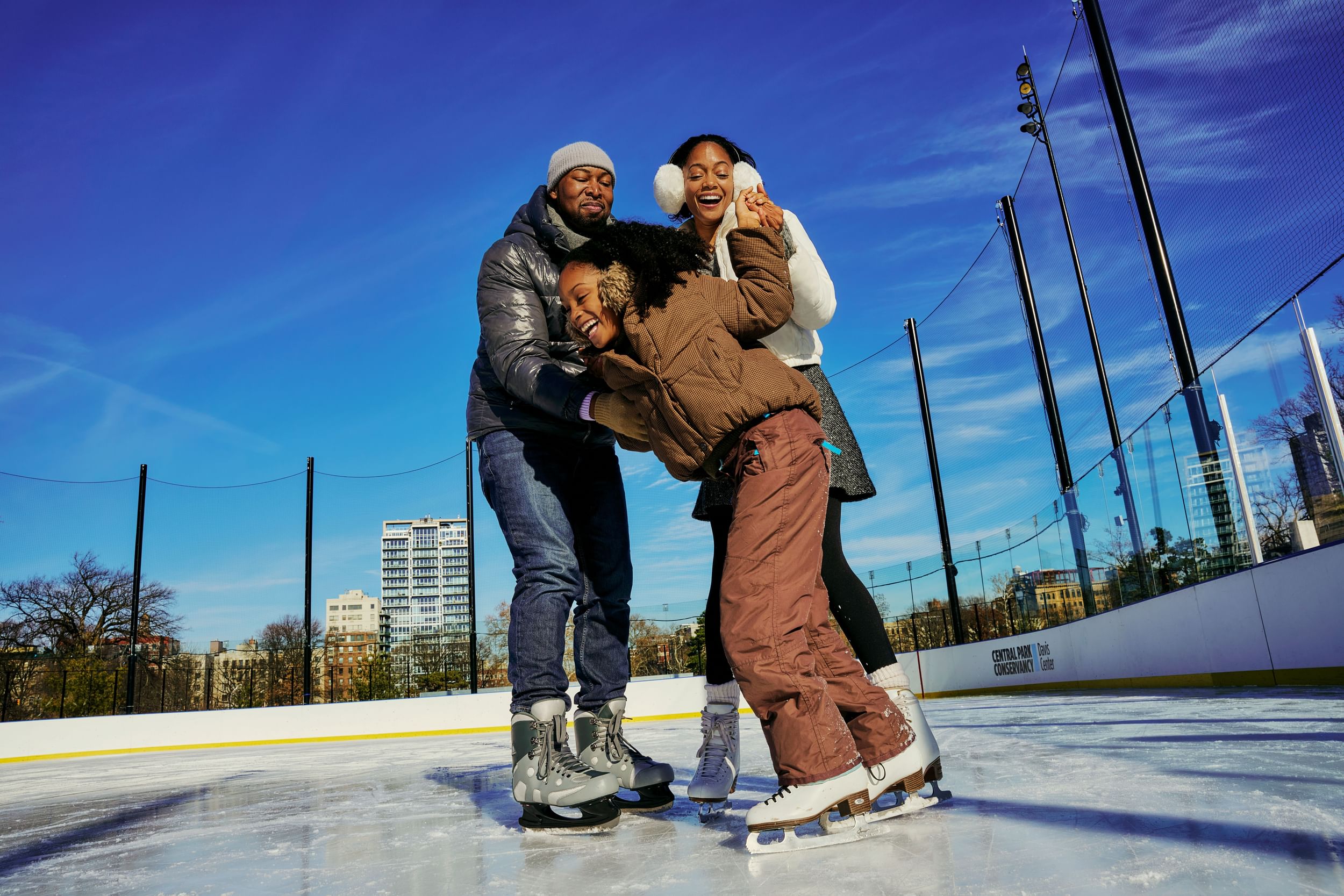 Laughing family hold on to each other while ice skating at the Davis Center