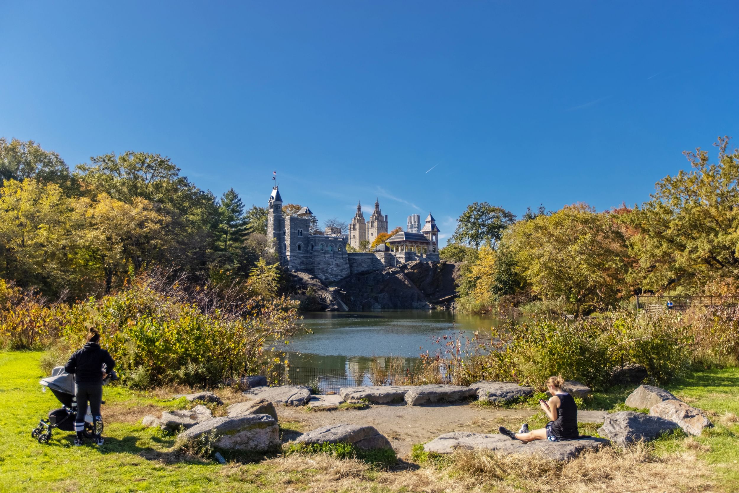 A person with a baby stroller stands next to the Turtle Pond at Belvedere Castle, Central Park, NYC