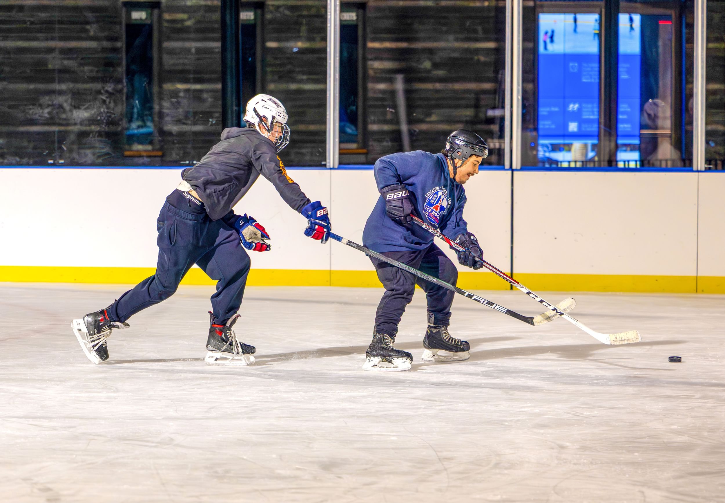 Two hockey players passing a puck around on the ice rink.