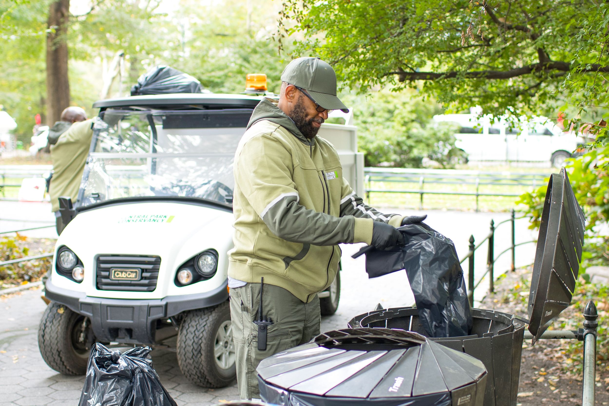 A Conservancy staff member, dressed in the organization's green uniform and hat, puts a new garbage bag in one of Central Park's receptacles.