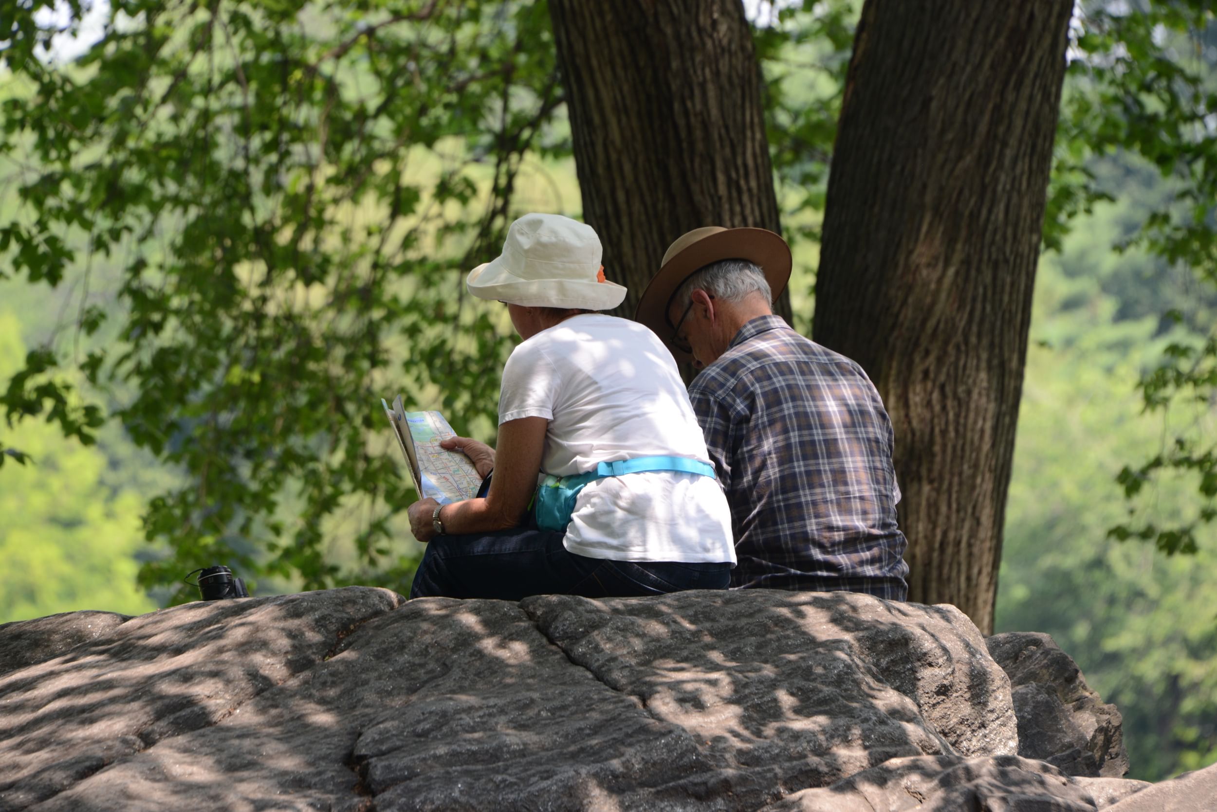 Two people sitting on a rock facing away from us, in Central Park, NYC