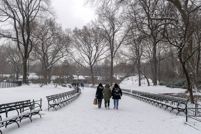 Three parkgoers bundled up for winter walk a snowcovered, bench-lined path in the Park